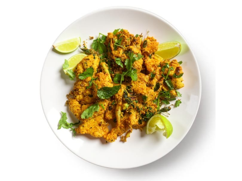 A white plate holds golden-brown spiced chicken pieces garnished with fresh cilantro and lime wedges.