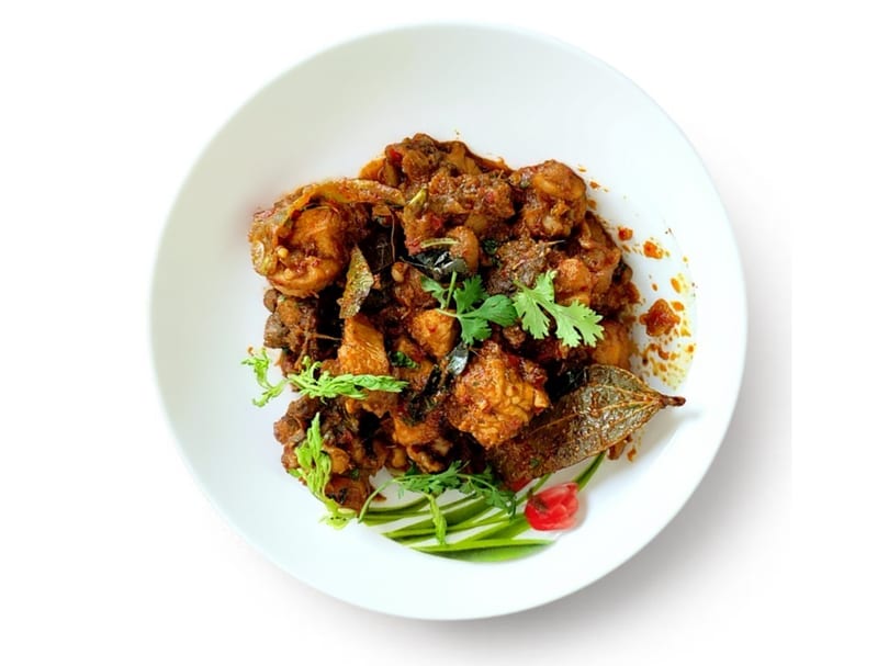 Spicy chicken curry with cilantro and bay leaf garnish on a white plate.