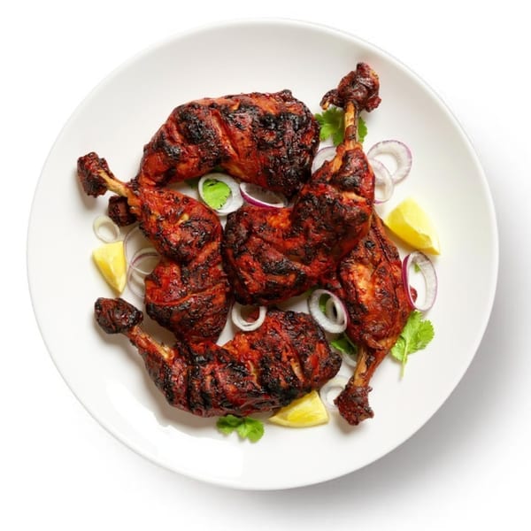 Tandoori chicken drumsticks and thighs, garnished with red onion, lemon wedges, and cilantro on a white plate.