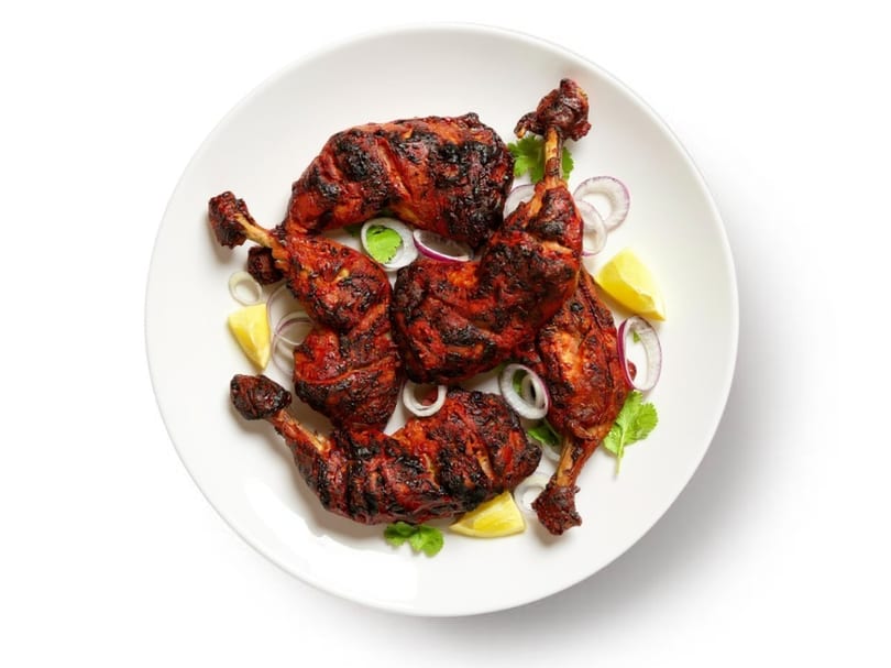 Tandoori chicken drumsticks and thighs, garnished with red onion, lemon wedges, and cilantro on a white plate.