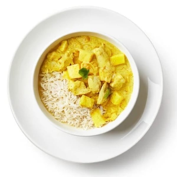 Overhead view of a white bowl filled with yellow curry, rice, and cilantro on a white plate.