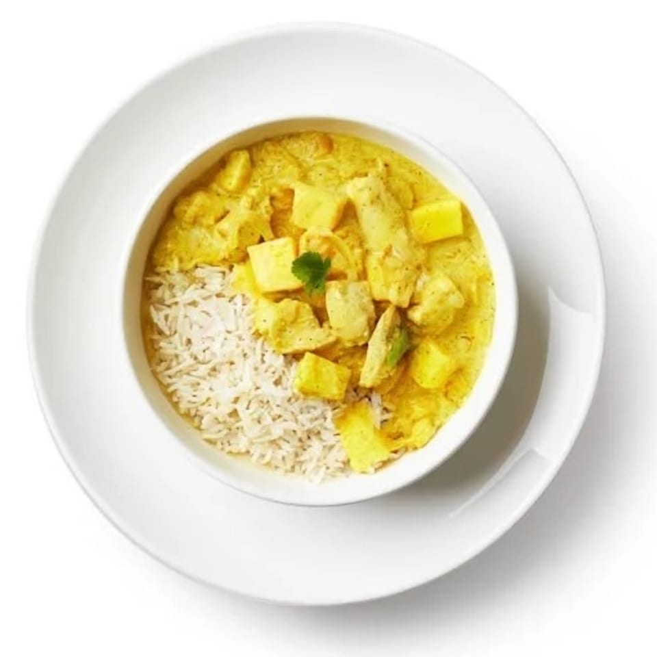 Overhead view of a white bowl filled with yellow curry, rice, and cilantro on a white plate.