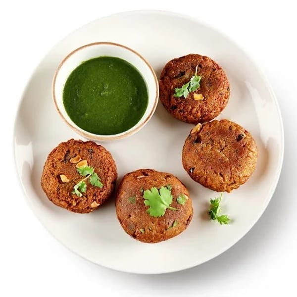 Four golden-brown lentil fritters with cilantro garnish, served with a bowl of green chutney.