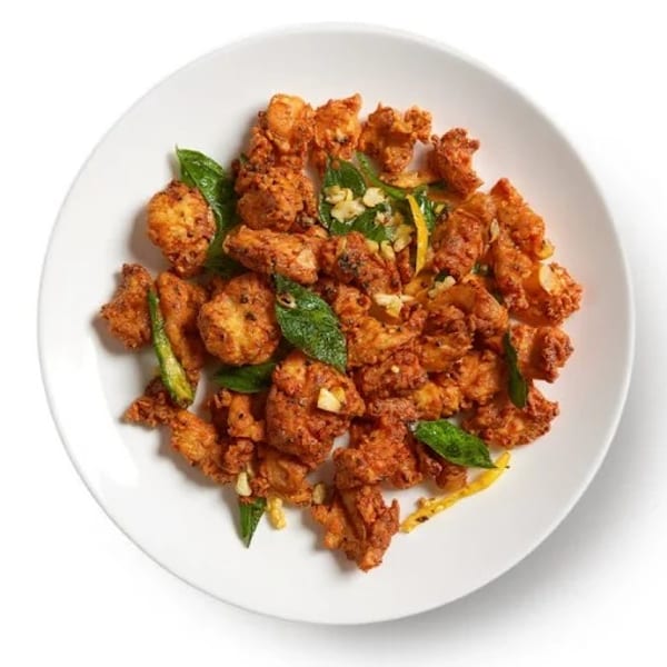 Crispy fried chicken pieces with green herbs and yellow strips on a white plate.