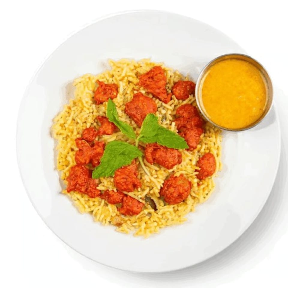 Chicken tikka biryani with a side of curry sauce, garnished with fresh mint leaves.