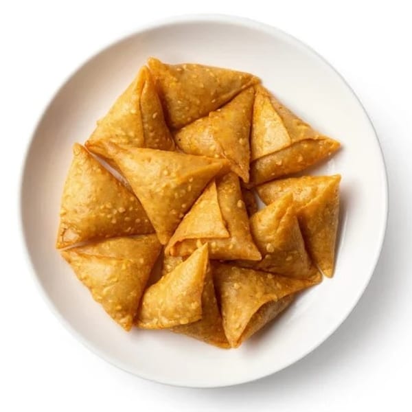 A white plate filled with golden-brown, triangular mini samosas, sprinkled with sesame seeds.