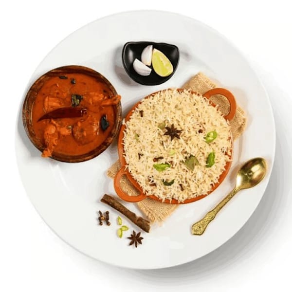 Chicken curry, rice, and spices on a white plate with a golden spoon.