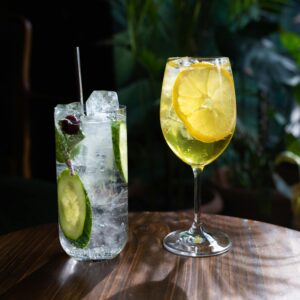 Two refreshing cocktails with cucumber and lemon garnish on a wooden table.